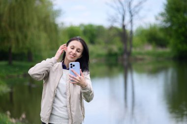 Gülümseyen kadın parkta video görüşmesi yapıyor ve yukarı doğru işaret ediyor..