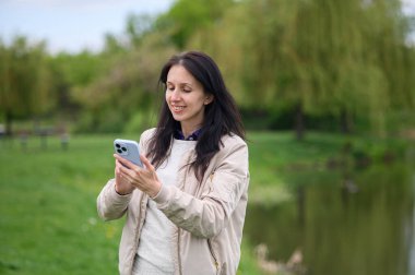 Gülümseyen kadın parkta video görüşmesi yapıyor ve yukarı doğru işaret ediyor..