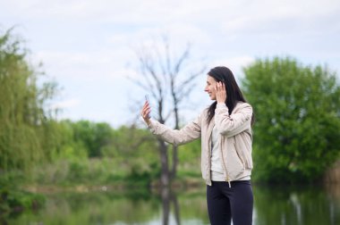 Gülümseyen kadın parkta video görüşmesi yapıyor ve yukarı doğru işaret ediyor..