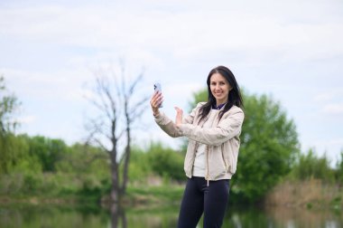 Gülümseyen kadın parkta video görüşmesi yapıyor ve yukarı doğru işaret ediyor..