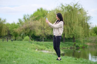 Gülümseyen kadın parkta video görüşmesi yapıyor ve yukarı doğru işaret ediyor..