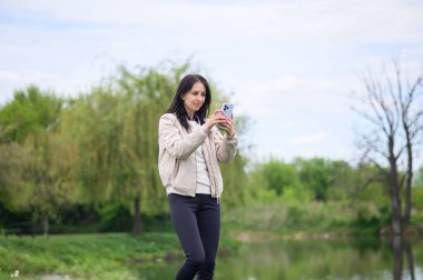 Gülümseyen kadın parkta video görüşmesi yapıyor ve yukarı doğru işaret ediyor..