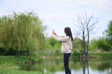 Gülümseyen kadın parkta video görüşmesi yapıyor ve yukarı doğru işaret ediyor..