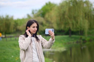 Gülümseyen kadın parkta video görüşmesi yapıyor ve yukarı doğru işaret ediyor..