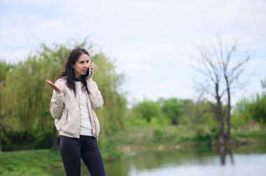 Gülümseyen kadın parkta video görüşmesi yapıyor ve yukarı doğru işaret ediyor..
