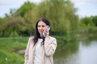 Gülümseyen kadın parkta video görüşmesi yapıyor ve yukarı doğru işaret ediyor..