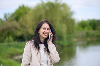 Gülümseyen kadın parkta video görüşmesi yapıyor ve yukarı doğru işaret ediyor..