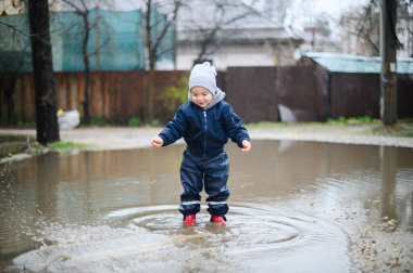 Yağmurlu su birikintisine atlayan Mutlu Çocuk Su geçirmez kıyafetlerle eğleniyor..