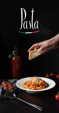 Domates soslu ve parmesanlı makarna. Makarna kelimesinin geçtiği siyah arka planda spagetti ile beyaz tabak. Makarnada parmesan peyniri rendeleyen eller. Geleneksel İtalyan yemekleri 