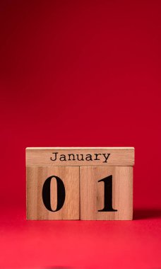 Kırmızı zemin üzerinde 1 Ocak tarihli ahşap takvim. Noel ve Yeni Yıl kutlaması konsepti. Tebrik kartı. Boşluğu kopyala, seçici odak