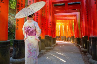Geleneksel Kimono elbiseli genç Japon kadın, binlerce torii kapısından oluşan bir yolun simgesi olan Fushimi Inari-taisha türbesinin senbon torii kapılarında geziniyor.