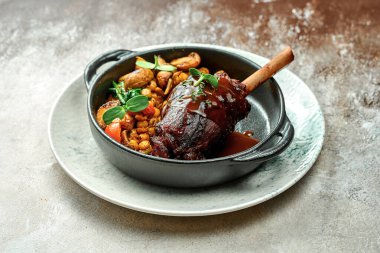 Tabakta sebzelerle birlikte koyu bir sosta pişirilmiş kuzu incik. Yakın çekim, seçici odaklanma.