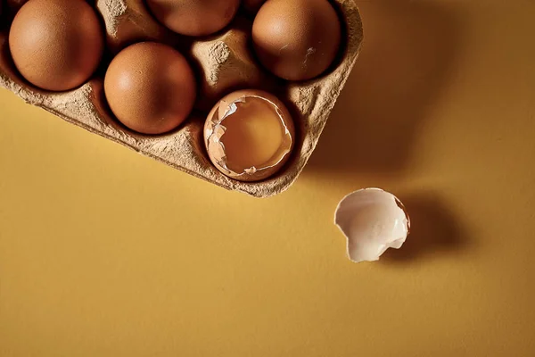 The poster concept is not like everyone else\'s. A broken egg in a cardboard package with other eggs. Yellow background, selective focus. Close-up