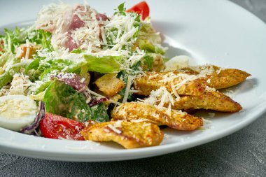 Classic caesar salad with sauce, grilled chicken and vegetables in a white plate. Concrete background
