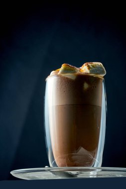 Cocoa or hot chocolate in a transparent glass with burnt marshmallows on a concrete background