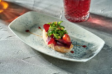 Vegetarian bruschetta with beets, tomatoes and arugula in a plate on a concrete background.
