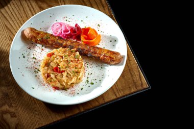 Bavyera usulü et sosisi, yahnili lahana turşusu, ahşap bir tabakta soğan.