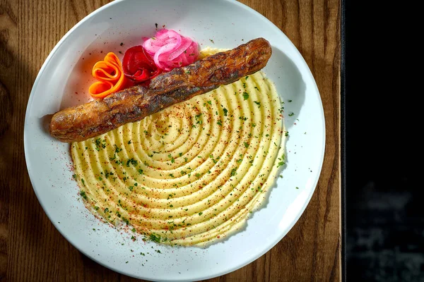 stock image Bavarian meat sausage with a garnish of mashed potatoes, onions in a plate on a wooden background. bratwurst