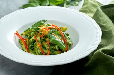 Gri arka planda beyaz tabakta ıspanaklı ve biberli vejetaryen makarna.