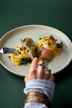 Kadın eli tabakta somonla Benedict yumurtası kesiyor.