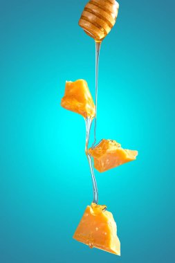 Uçan peynir parçaları mavi arka planda bal ile doldurulur. Yiyecekler havada uçuşuyor.