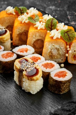 Kara tahtada farklı suşi ruloları. Japon suşisi, somon, yılan balığı, karides.