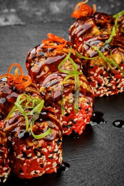 Tobiko havyarında pişmiş suşi rulosu ve siyah arka planda yılan balığı. Japon yemeği, menü için fotoğraf