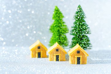 Üç minyatür kulübe ve ışıltılı bir arka planda iki oyuncak Noel ağacı..