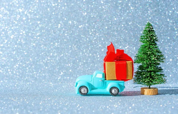 stock image Miniature retro pickup truck model with a huge christmas present parked by a toy new year tree against a sparkling winter background.