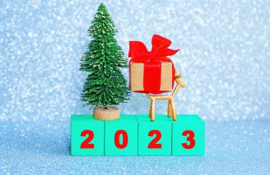 Minyatür pırıl pırıl yeni yıl 2023 arkaplanı yeşil tahta harf bloklarından, oyuncak noel ağacından, küçük geyik heykelciğinden ve süslü hediye kutusundan düzenlenmiş..