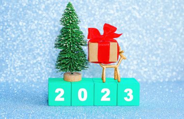 Minyatür pırıl pırıl yeni yıl 2023 'ten itibaren yeşil tahta harf bloklarından, oyuncak Noel ağacından, küçük geyik heykelciğinden ve süslü hediye kutusundan yapılmış..