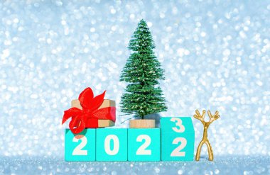 2022 'den 2023' e geçiş dönemi. Tahta bloklar, oyuncak noel ağacı, küçük geyik heykelciği ve süslenmiş hediye kutusu ile göz alıcı bir arkaplan taklit karına karşı..