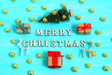 Oyuncak Noel ağacı, geyik heykelcikleri, dekorasyon topları ve mavi ahşap arka planda paketlenmiş hediye kutularıyla dolu canlı mutlu tatil reklamları..