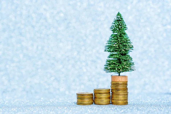 stock image Giving up Christmas due cost of living crisis: Miniature toy Christmas tree placed on a pile of coins against a glittering background imitating snowing.