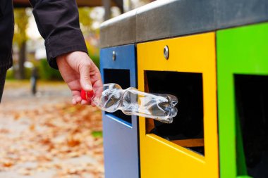 Parktaki sarı çöp kutusuna plastik şişe atan bir erkek. Sorumlu atık sıralama, toplama ve geri dönüşüm kavramı.