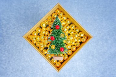 Arkaplanda altın renkli toplarla dolu bir kutuda süslü minyatür Noel ağacı..