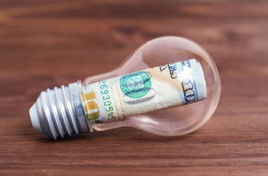 100 dolarlık banknot, ahşap bir arka planda izole edilmiş bir ampulün içinde yuvarlandı. Yaratıcı iş fikri kavramı.