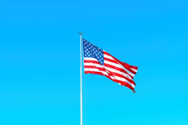 American flag in motion waving freely against a clear blue sky symbolizing freedom and democracy. American spirit representation for a political campaign or a community event.
