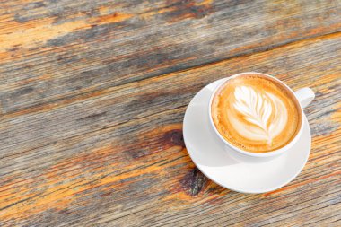 The moment of peace and relaxation: perfectly crafted cup of coffee with latte art on the creamy foam placed on a rustic wooden table with copy space.