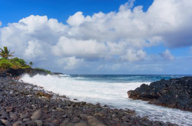 Scenic view of the Hawaii's rocky coastline with contrasting colors of the rocks and turquoise water against the blue sky with rich white clouds. Nature or travel-themed design concept.