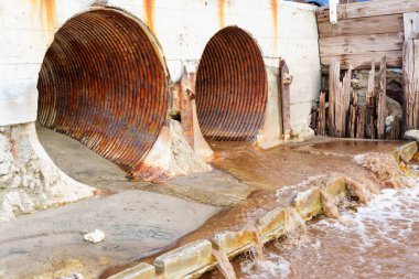 Elements of the Malibu Beach drainage system designed to efficiently manage excess water. Water running through large rusty pipes.