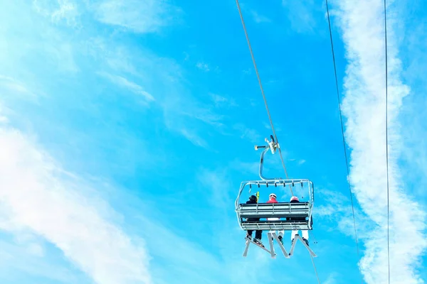 在阳光明媚的日子里 一群滑雪者乘坐滑雪车迎着晴朗的蓝天飞驰而上 从下面向后看去 — 图库照片