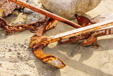 Kumsalda eski, paslı bir çapa ve zincirler sahilin engebeli güzelliğini yakalıyor..