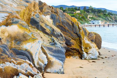 Muazzam bir kaya oluşumu, rıhtım ve Malibu, California 'daki tepelerde evleri ile göz kamaştırıcı bir okyanus manzarası. Kaliforniya kıyı şeridinin çarpıcı manzarası.