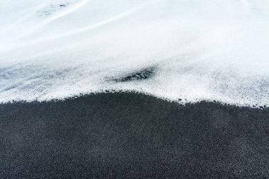 Beyaz köpüklü dalga yavaşça siyah bir kumsalı kaplıyor. Yaratıcı barış, uyum ve denge kavramı.