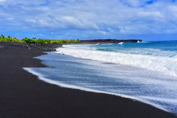 Beauty of a black sand beach on the ocean shore in Hawaii. Contrasting colors of black sand and blue ocean create a mesmerizing composition, while the lush greenery adds a touch of tropical paradise.
