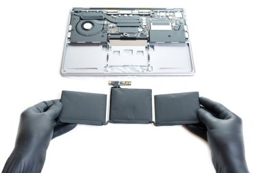 Siyah eldivenli eller, laptoptan yeni çıkarılmış şişmiş bir pil tutuyor..
