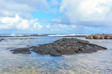 Hawaii 'deki Idyllic plajı, bulutlu bir gökyüzü tarafından çerçevelenmiş sonsuz bir okyanusa uzanan sakin bir volkanik kaya ufku..