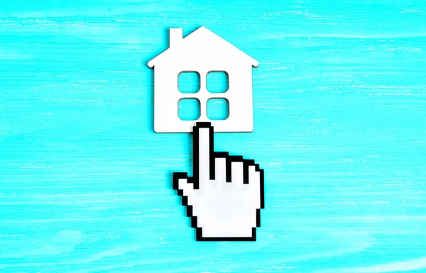 Plastic hand-shaped mouse cursor figurine clicking a flat house shape placed on a blue wooden background, representing the idea of building appealing and intuitive graphical interfaces.