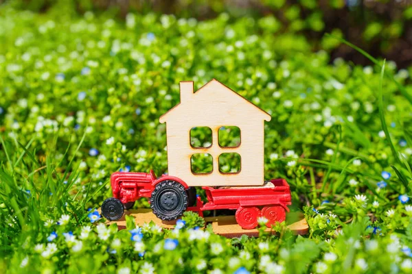 stock image The essence of countryside living in the springtime, with a toy tractor carrying a miniature flat house perched on a flowerbed of green grass and colorful flowers.